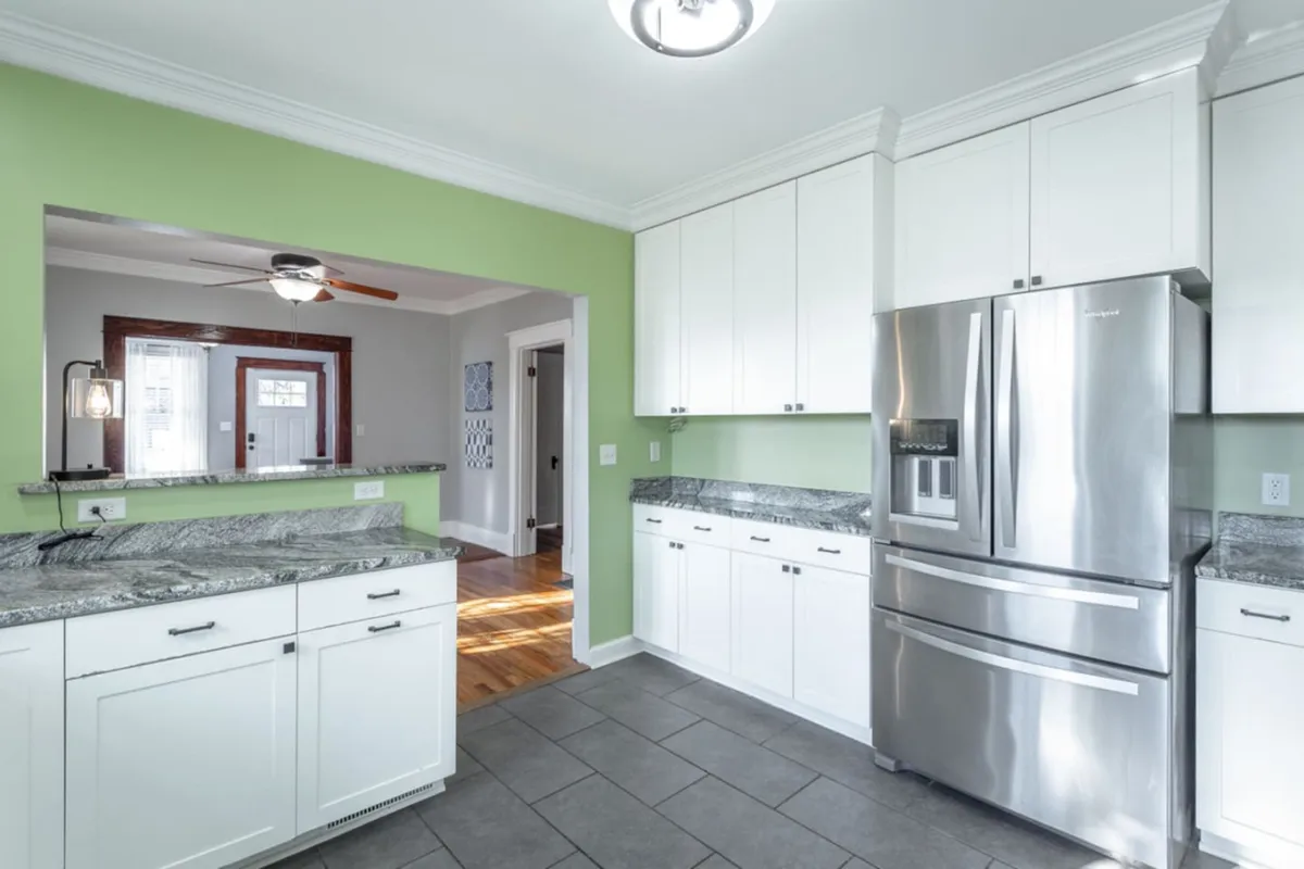 This image features a bright, cheerful kitchen with a stainless steel refrigerator, granite countertops, and a green accent wall. The space is well-lit and designed for both cooking and entertaining, with plenty of counter space for group meal prep or casual gatherings.