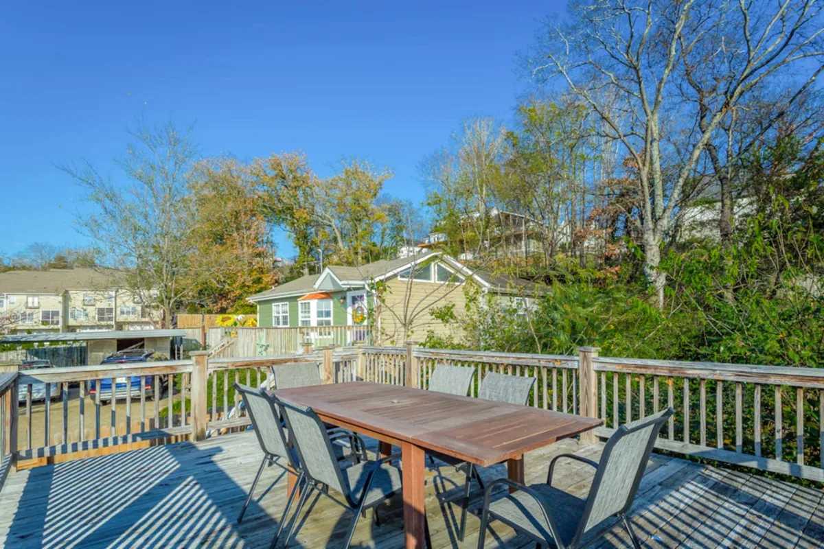 An outdoor dining area surrounded by leafy trees and neighboring houses, with a table set for gathering. The mood is cheerful, and the space is ideal for sunset dinners, morning coffee, or weekend family barbecues.