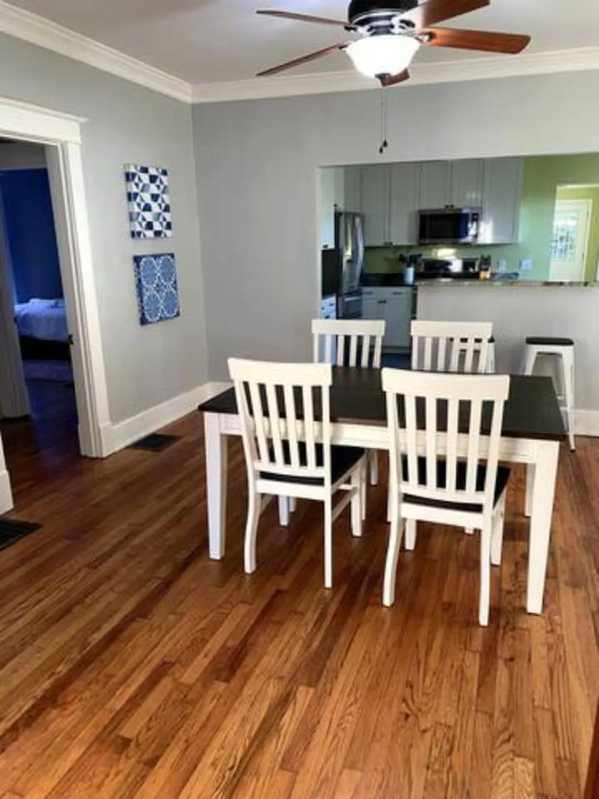 A spacious dining area featuring a large dining table surrounded by chairs, warm wall art, and a view into the adjacent kitchen. The setup is ideal for communal meals and group gatherings.