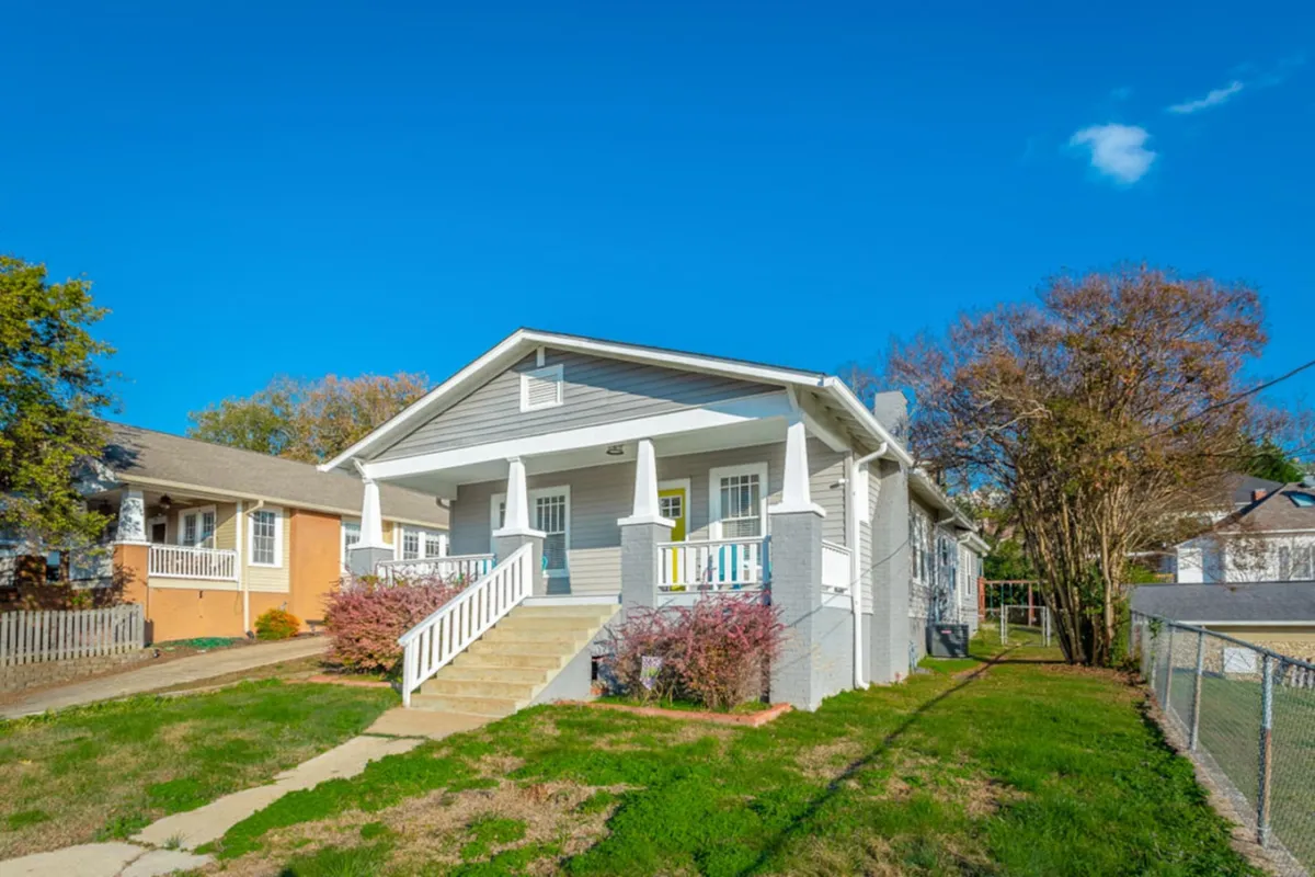 This image captures the welcoming front porch of the property, surrounded by a landscaped yard and vibrant shrubs. The scene suggests a space perfect for outdoor gatherings, relaxing with a group, or enjoying a sunset after a day of adventure.