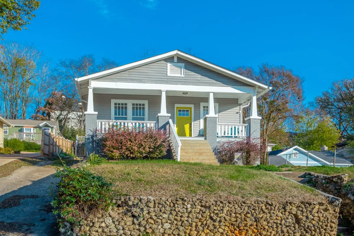 A vibrant exterior shot focused on a bright yellow front door, a well-manicured lawn, and an inviting porch with white railings, perfect for casual gatherings or relaxing evenings. The image exudes warmth and Southern hospitality.
