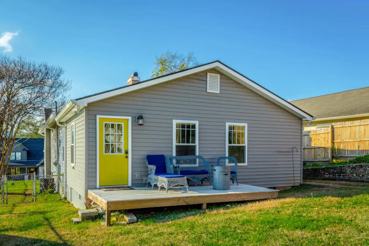 A welcoming deck with a yellow door features comfortable outdoor seating surrounded by garden landscaping. The area is bathed in warm natural light, inviting guests to unwind, socialize, and enjoy the garden and sunset views from the comfort of the porch.