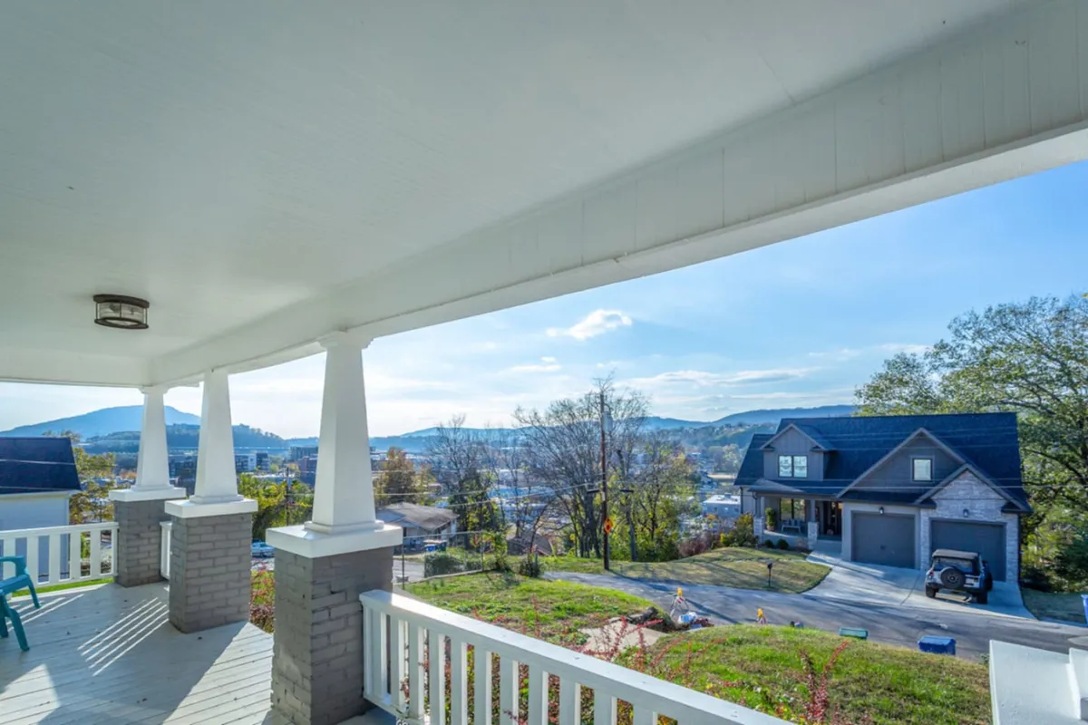 The image showcases a spacious porch overlooking rolling mountains, capturing a tranquil sunrise. The porch is inviting for gatherings, with neighboring houses visible in the distance, reinforcing a sense of community. The scene hints at relaxation, socializing, and enjoying peaceful views, with the promise of stargazing or seasonal celebrations.